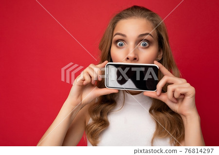 Amazed surprised attractive young blonde female person wearing white t-shirt isolated on red 76814297
