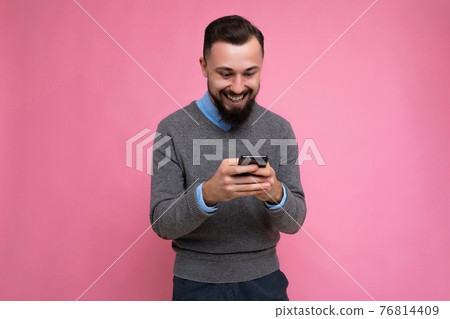 Positive smiling handsome good looking brunet bearded young man wearing grey sweater and blue shirt 76814409