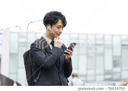A man in his early thirties wearing headphones looking at the screen of his smartphone 76814703