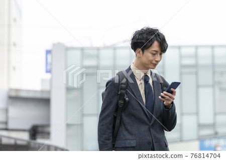 A man in his early 30s looking at a smartphone screen 76814704