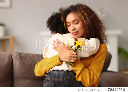 Young mixed race woman mother with flower bouquet embracing son while getting congratulations on Mother's day Young mixed race woman mother with flower bouquet embracing son while getting congratulations on Mother's day 76814930