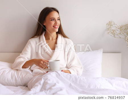 Happy woman enjoying hot drink in bed 76814937
