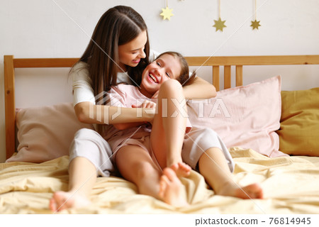 Young beautiful mom with happy little child embracing and expressing love while sitting together on the bed 76814945