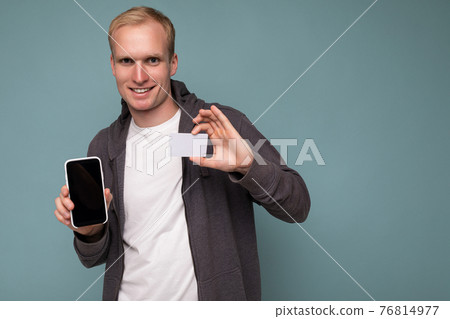 Handsome smiling blonde man wearing grey sweater and white t-shirt isolated over blue background 76814977