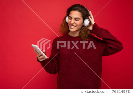 Shot of beautiful emotional young brunette curly woman wearing dark red sweater isolated over red Shot of beautiful emotional young brunette curly woman wearing dark red sweater isolated over red 76814978