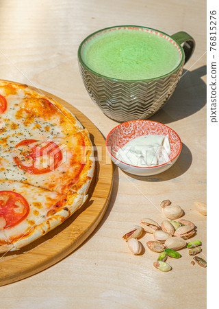 Japanese iced Matcha latte tea with pizza margherita and pistachios on wooden table. 76815276