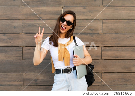 Beautiful smiling charming young brunet woman looking at camera holding computer laptop and Beautiful smiling charming young brunet woman looking at camera holding computer laptop and 76815660