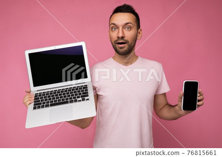 Handsome amazed man holding laptop computer and mobile phone looking at camera in t-shirt on Handsome amazed man holding laptop computer and mobile phone looking at camera in t-shirt on 76815661