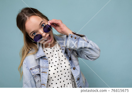 Shot of pretty positive joyful young blonde woman wearing blue jean jacket and stylish sunglasses 76815675