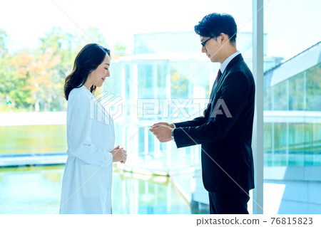 Medical image of a female doctor in a white coat and a male MR in a suit exchanging business cards at a hospital 76815823