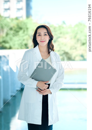 A female doctor with a smiling computer in a lab coat at the hospital A female doctor with a smiling computer in a lab coat at the hospital 76816194