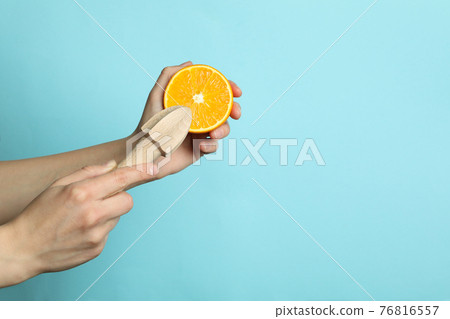Female hands hold orange and juicer on blue background Female hands hold orange and juicer on blue background 76816557