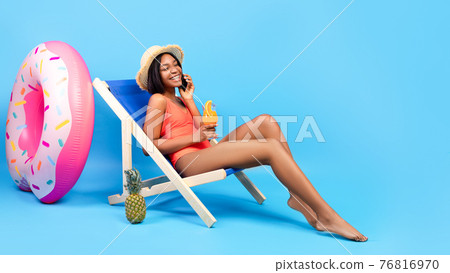 Sweet black woman in swimsuit enjoying summer cocktail, speaking on smartphone over blue background, panorama Sweet black woman in swimsuit enjoying summer cocktail, speaking on smartphone over blue background, panorama 76816970