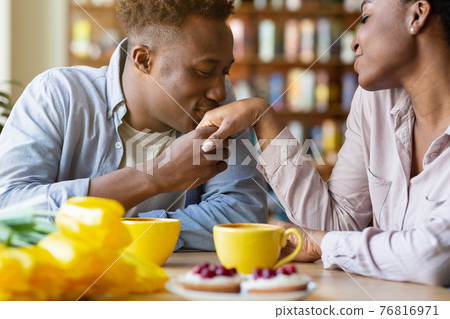 Romantic young man kissing his beloved woman's hand on festive Valentine's dinner at cozy cafe Romantic young man kissing his beloved woman's hand on festive Valentine's dinner at cozy cafe 76816971
