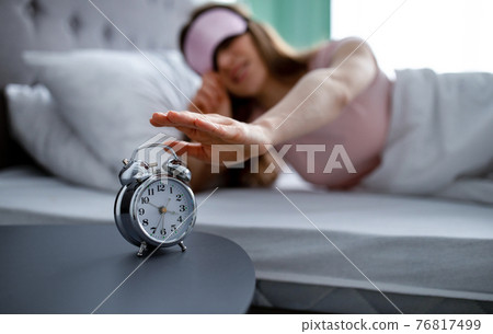 Young woman in sleep mask turning off alarm clock in morning, selective focus 76817499