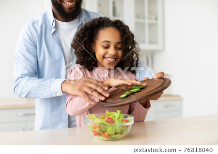 Cheerful afro father and daughter cooking salad together Cheerful afro father and daughter cooking salad together 76818040