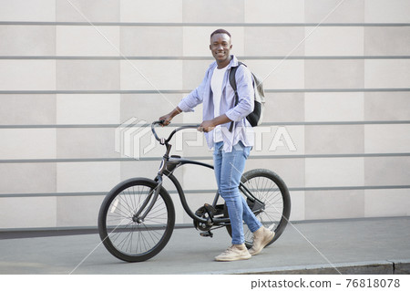 Handsome black guy with backpack and modern bike near brick wall on city street 76818078