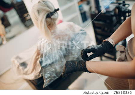 Young woman hairdresser puts on gloves and preparing dying hair at beauty salon. Professional hair roots coloring 76818386