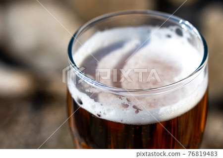 Light beer in a glass goblet on the background of firewood. Rest in the country. Beer foam in the sunlight 76819483