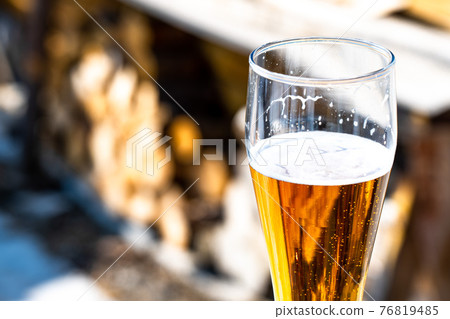 Light beer in a glass goblet on the background of firewood. Rest in the country. Beer foam in the sunlight 76819485