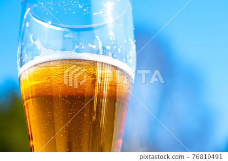 Light beer in a glass goblet on a background of blue sky. Beer foam on the walls of a glass in the sunlight. 76819491