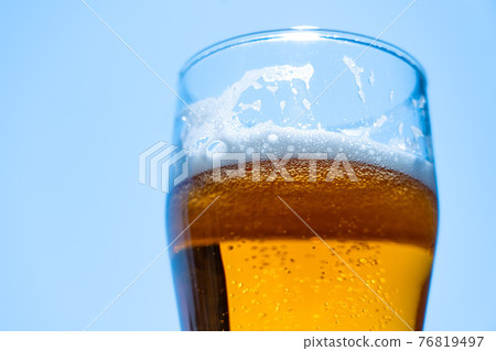 Light beer in a glass goblet on a background of blue sky. Beer foam on the walls of a glass in the sunlight. 76819497