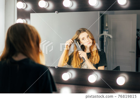 Young cute girl teen using a hair straightener on her wavy red hair Young cute girl teen using a hair straightener on her wavy red hair 76819815