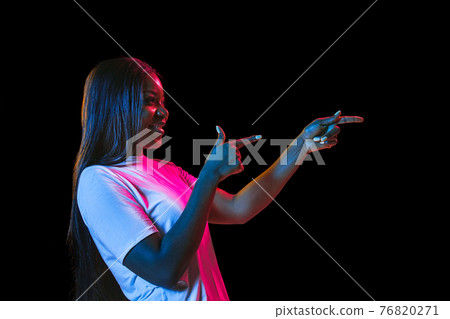 African young woman's portrait on dark studio background in neon. Concept of human emotions, facial expression, youth, sales, ad. 76820271