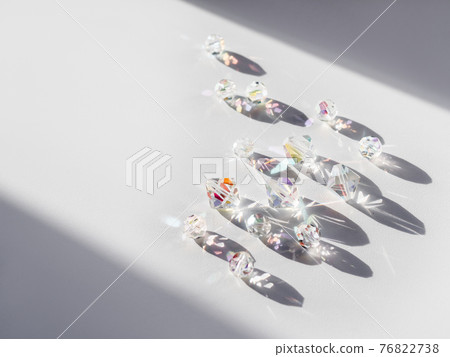 Sparkling glass beads on hard sunlight. Geometrical shadow and rainbow sun beams and reflections on transparent spangles. Jewellery on white background. Sparkling glass beads on hard sunlight. Geometrical shadow and rainbow sun beams and reflections on transparent spangles. Jewellery on white background. 76822738