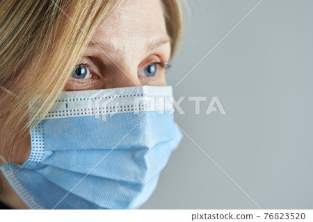Woman blonde wearing medical face mask on a gray background. Photo with copy space. 76823520