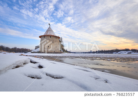 Ancient Pskov in winter. The Flat tower of the Pskov Kremlin against the blue sky. In the foreground, the river is covered with ice. Ancient Pskov in winter. The Flat tower of the Pskov Kremlin against the blue sky. In the foreground, the river is covered with ice. 76823557