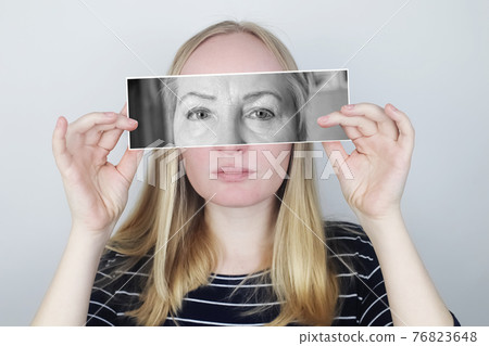 The girl holds a photograph of her old mother to her face. Aging, genetics, family tree and loss of youth concept. Before and after age-related changes. The girl holds a photograph of her old mother to her face. Aging, genetics, family tree and loss of youth concept. Before and after age-related changes. 76823648
