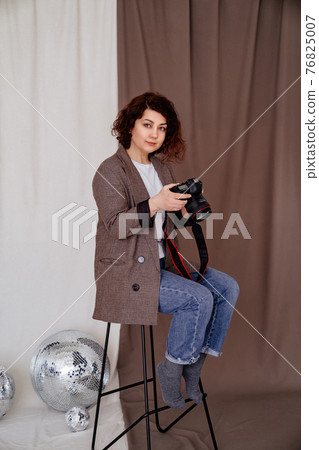 woman in jeans and checkered jacket on high chair in photo studio with camera 76825007