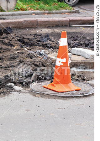 An orange traffic cone stands on the manhole and encloses the danger zone on the roadway. 76825378