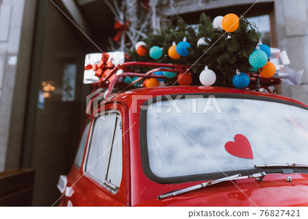 Red retro car with a Christmas tree fir tied to the roof. Red retro car with a Christmas tree fir tied to the roof. 76827421