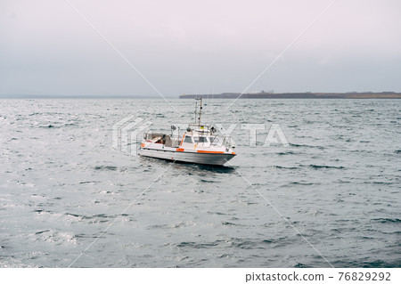 White fishing motor boat sails across the Atlantic Ocean in Iceland. Side view 76829292