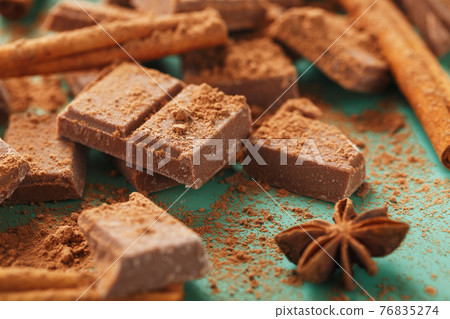 Chocolate broken into slices with cocoa powder and spices on a green background Chocolate broken into slices with cocoa powder and spices on a green background 76835274