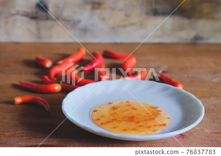 Red chili peppers and chili sauce in dish on wood table Red chili peppers and chili sauce in dish on wood table 76837783