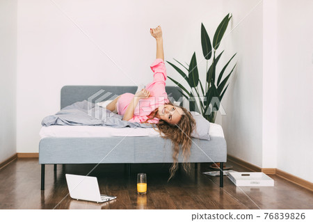 Beautiful blonde woman drinks juice in the morning in bed after waking up and enjoys the weekend Beautiful blonde woman drinks juice in the morning in bed after waking up and enjoys the weekend 76839826