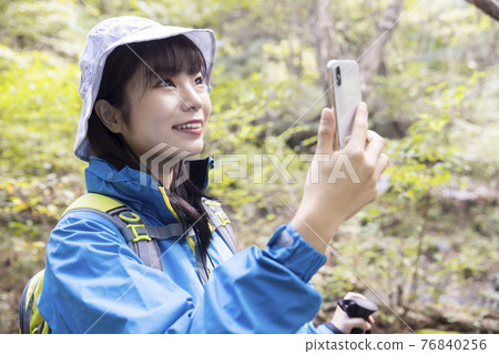 A woman trekking image taking a picture with a smartphone during trekking A woman trekking image taking a picture with a smartphone during trekking 76840256