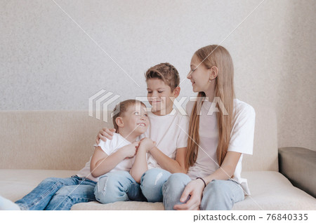 friendly happy children a girl and two boys are sitting on the sofa smiling looking at each other friendly happy children a girl and two boys are sitting on the sofa smiling looking at each other 76840335