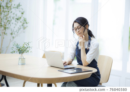 Woman in an apron looking at a computer Woman in an apron looking at a computer 76840380