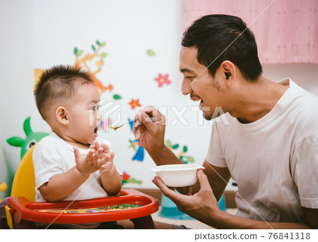 Father acting Mom feeding his son baby 1 year old on chair Father acting Mom feeding his son baby 1 year old on chair 76841318