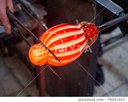 Hands shaping melted glass with long knife jack. Art and craft worker molding 76841923