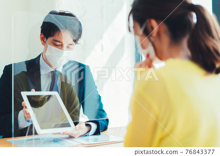 一個戴著面具的人通過丙烯酸板為客戶服務 76843377