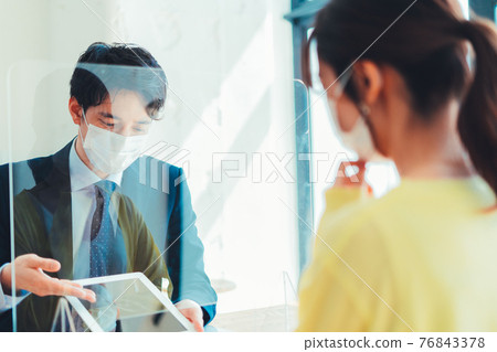 A man in a mask serving customers through an acrylic board 76843378