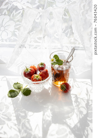 Cup of tea and wild strawberries on a white lace background 76843420