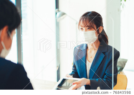 A woman in a mask serving customers through an acrylic board A woman in a mask serving customers through an acrylic board 76843598