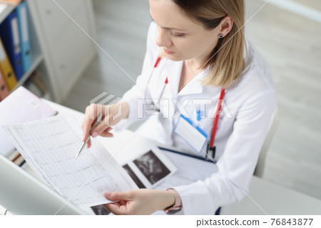 Doctor sitting at table and looking at cardiogram in clinic Doctor sitting at table and looking at cardiogram in clinic 76843877