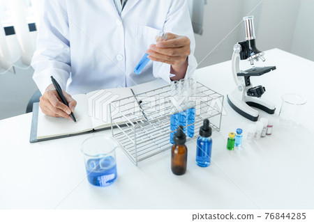 Scientist woman holding test tube in her hands and writing down result report on notebook while working 76844285